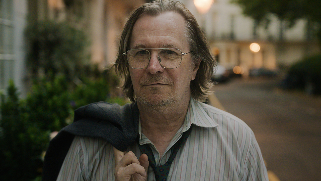 Gary Oldman souriant avec sa veste drapée sur son épaule dans Slow Horses sur Apple TV+.