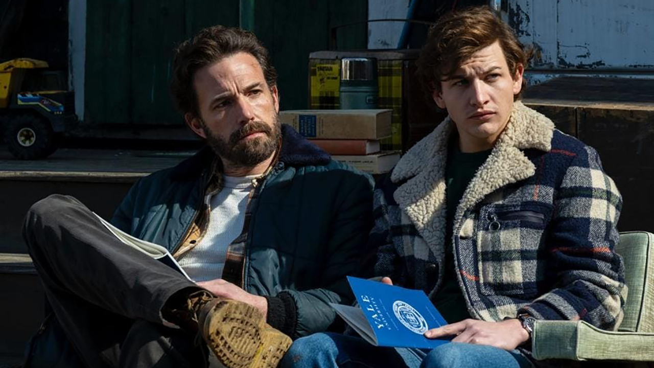 Ben Affleck y un joven se sientan juntos leyendo folletos de Yale en una escena de The Tender Bar.