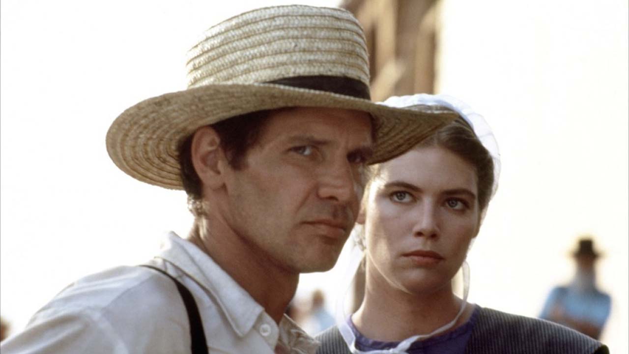 Harrison Ford in a straw hat with an Amish woman behind him in the movie Witness.