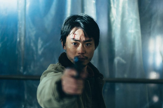 Masaki Suda aims his gun at the camera in a still from the movie Cloud.