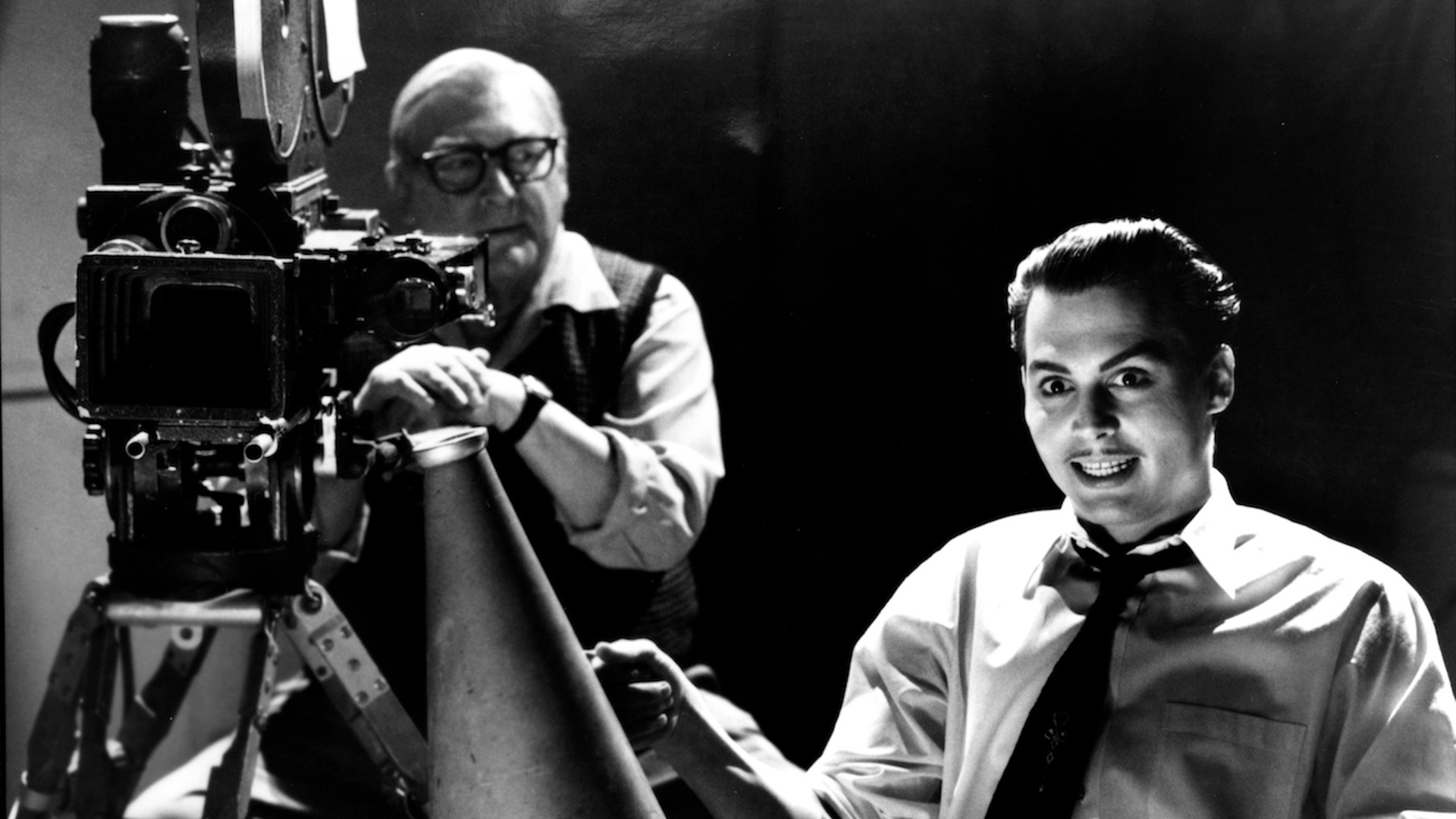 Johnny Depp grins with bug-eyed enthusiasm from the director's chair as a camera man glances at from nearby in a black-and-white still from the movie Ed Wood.