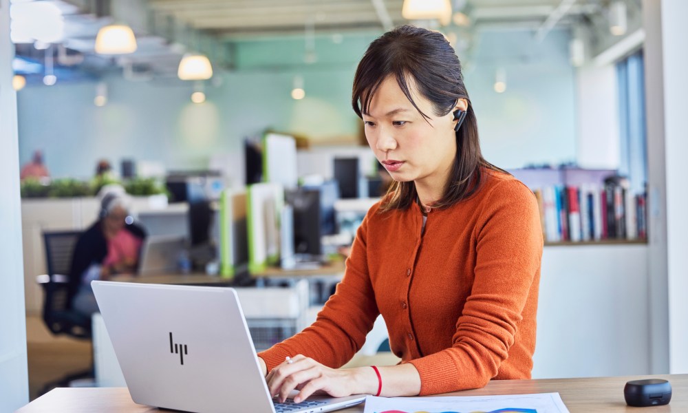 A woman sits at a desk, using the new HP EliteBook X.