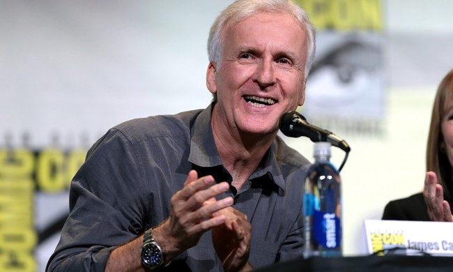 James Cameron claps his hands while sitting in front of a microphone.