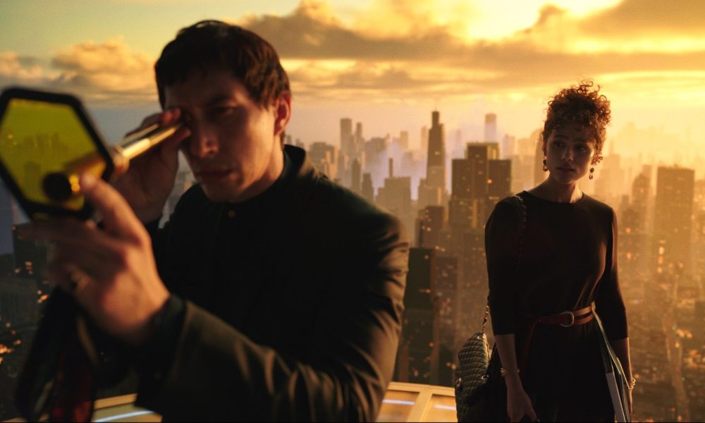 Adam Driver stares through a looking glass while Nathalie Emmanuel watches him atop a building in a still from the movie Megalopolis.