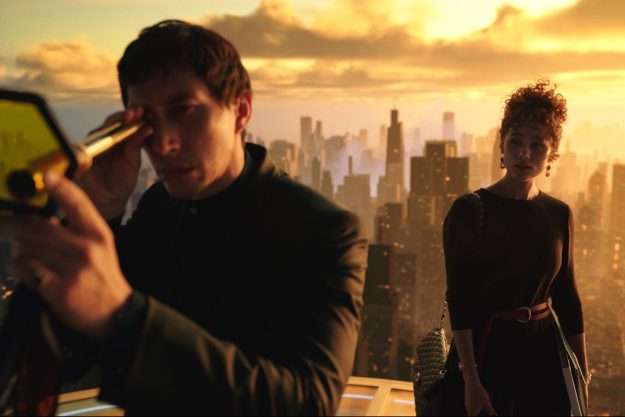 Adam Driver stares through a looking glass while Nathalie Emmanuel watches him atop a building in a still from the movie Megalopolis.