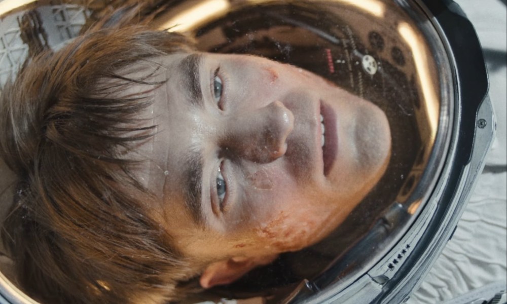 Robert Pattinson as an astronaut stares with a blank expression on his face.