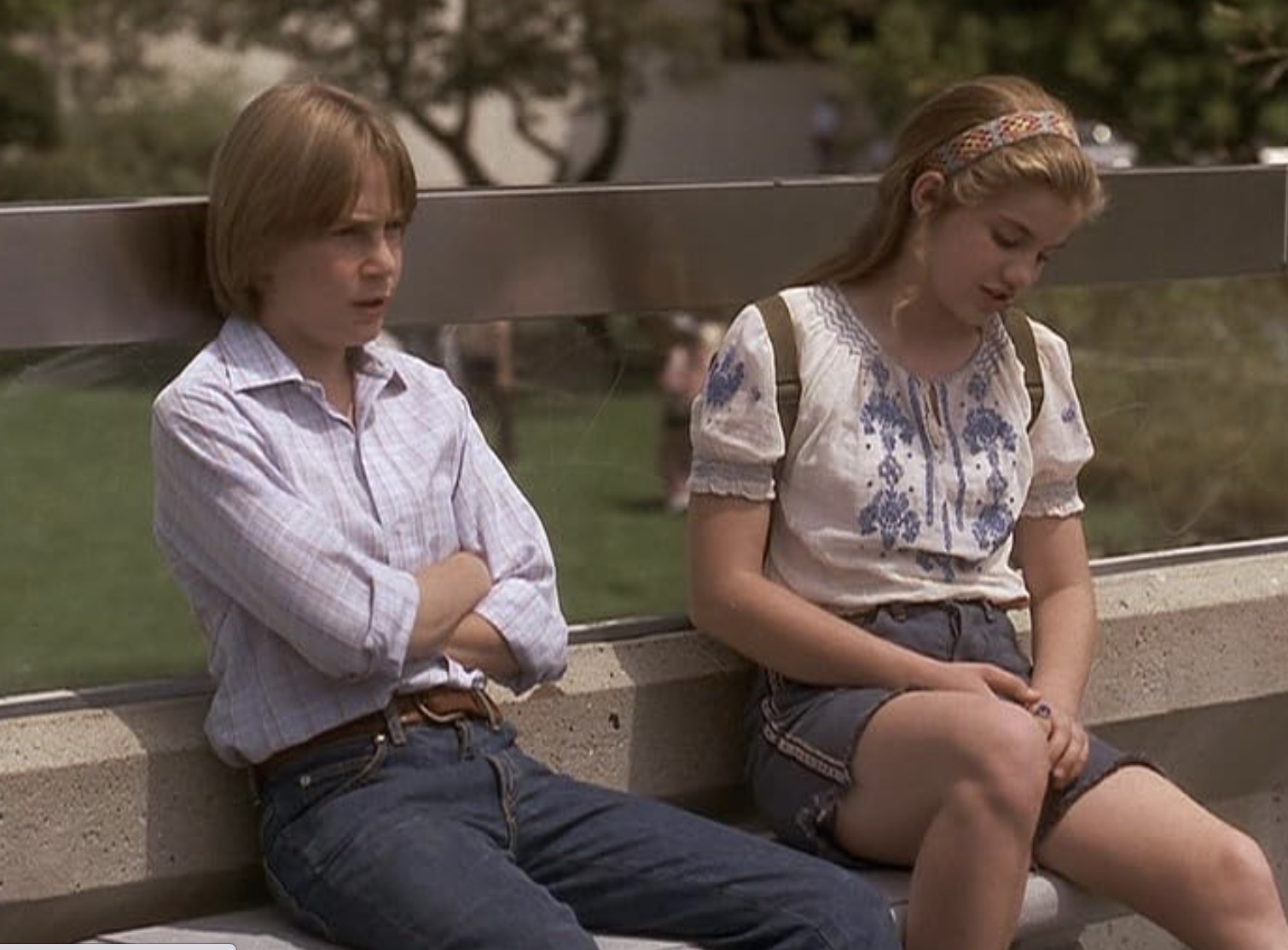 A boy and a girl sit next to each other on a bench.