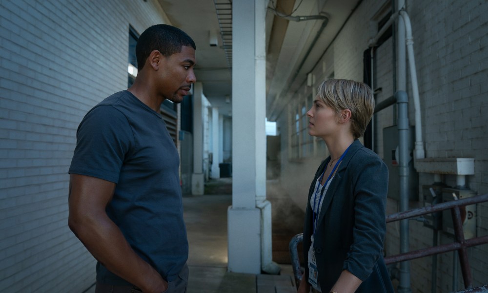 A woman and man stand across from each other in an alley.