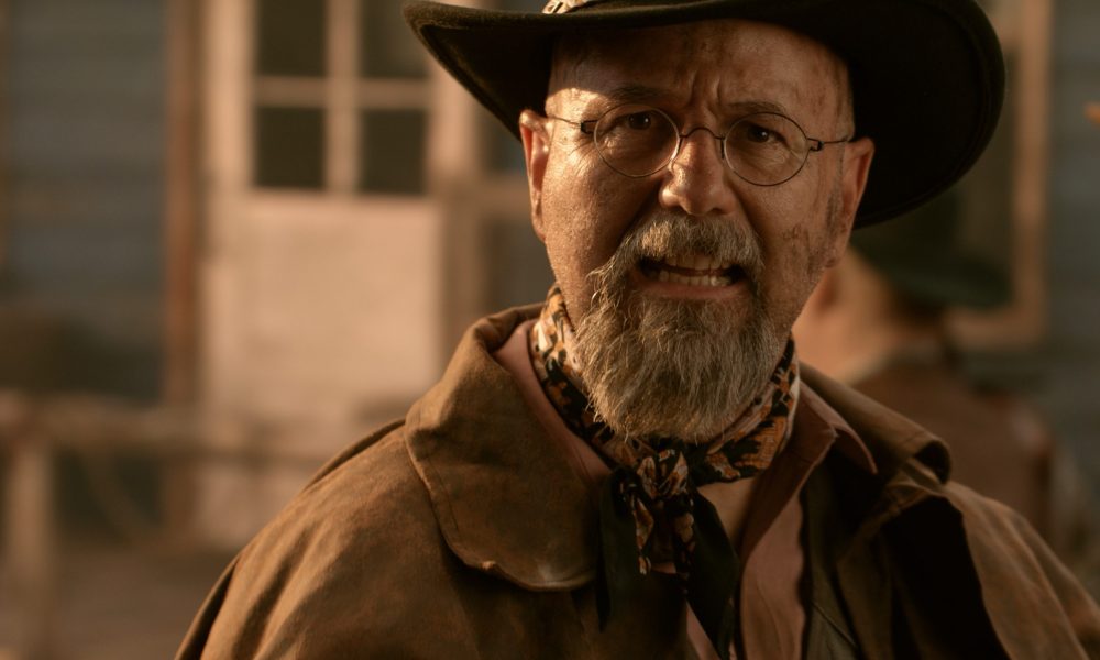 A man in a Cowboy hat smirks at the camera.