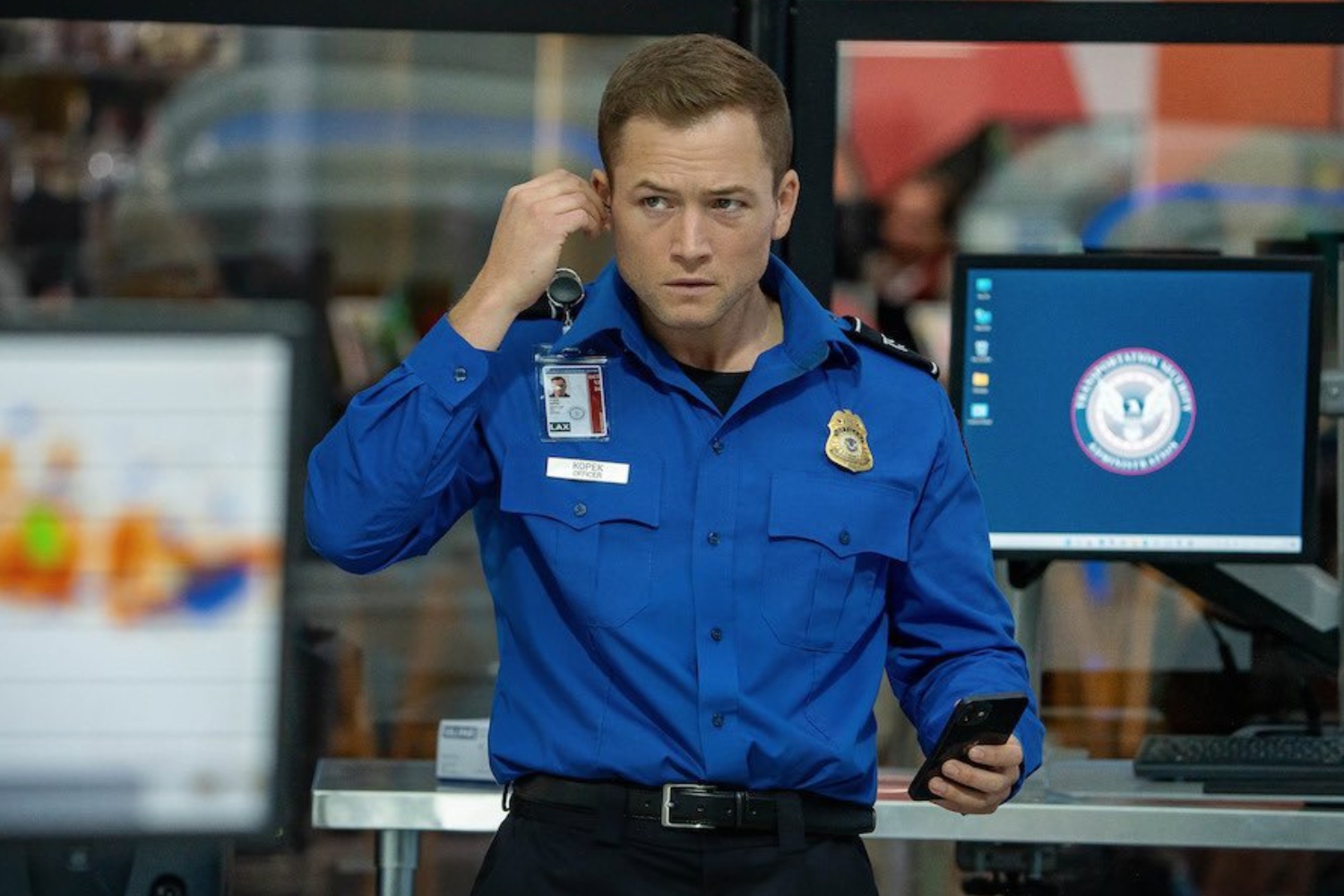 Un agent de la TSA lui met un écouteur à l'oreille.