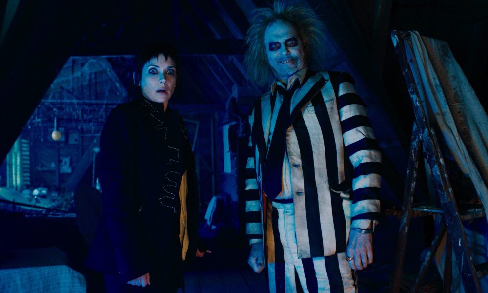 Winona Ryder stands next to Michael Keaton in Beetlejuice Beetlejuice.