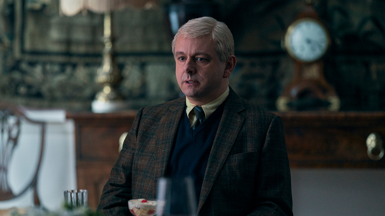 Michael Sheen dresses up as Prince Andrew and sits in a suit in a scene from A Very Royal Scandal.