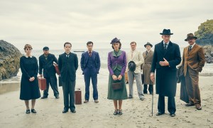 A group of people stand on a beach in And Then There Were None.