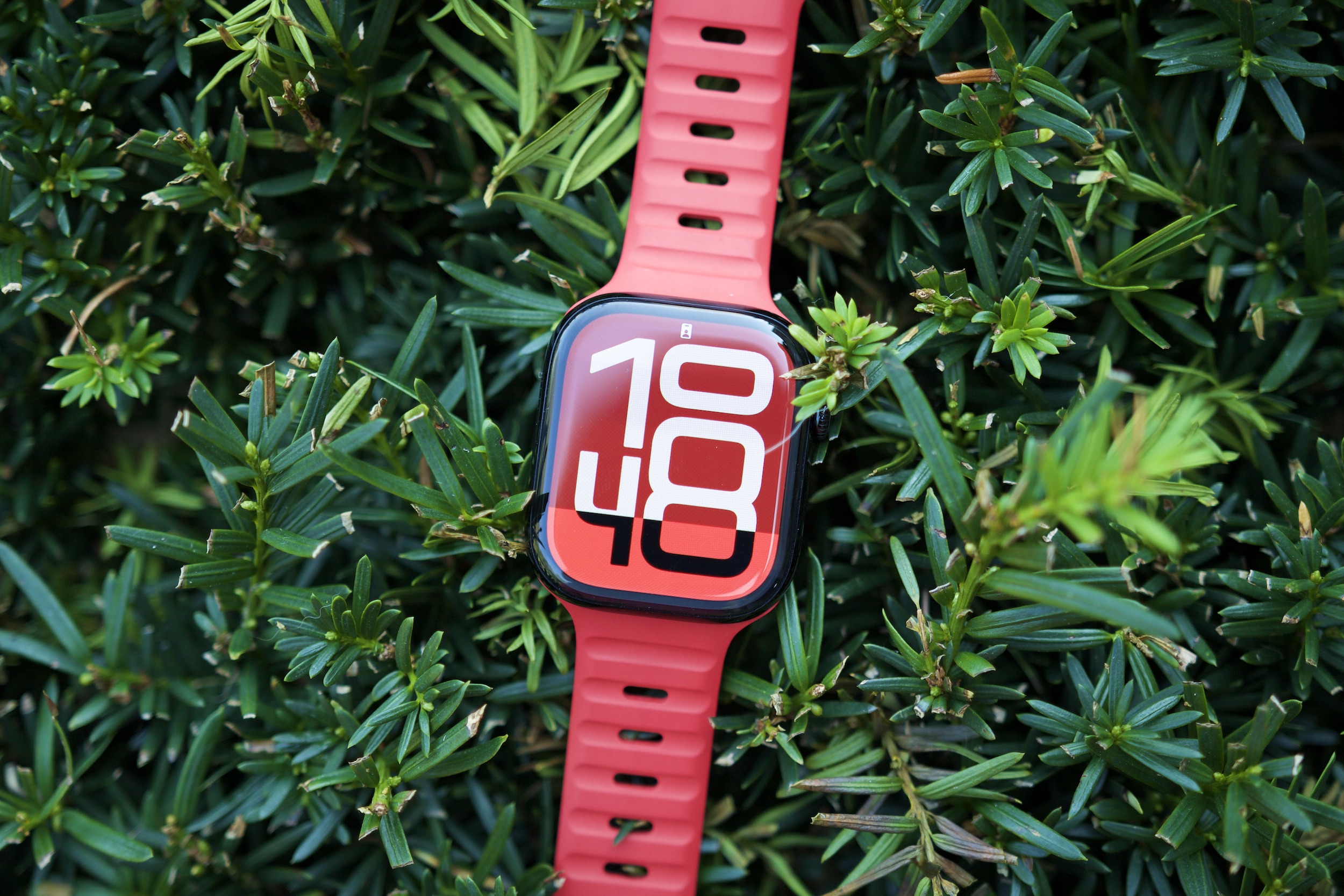 The Apple Watch Series 10 sitting on top of a green bush.