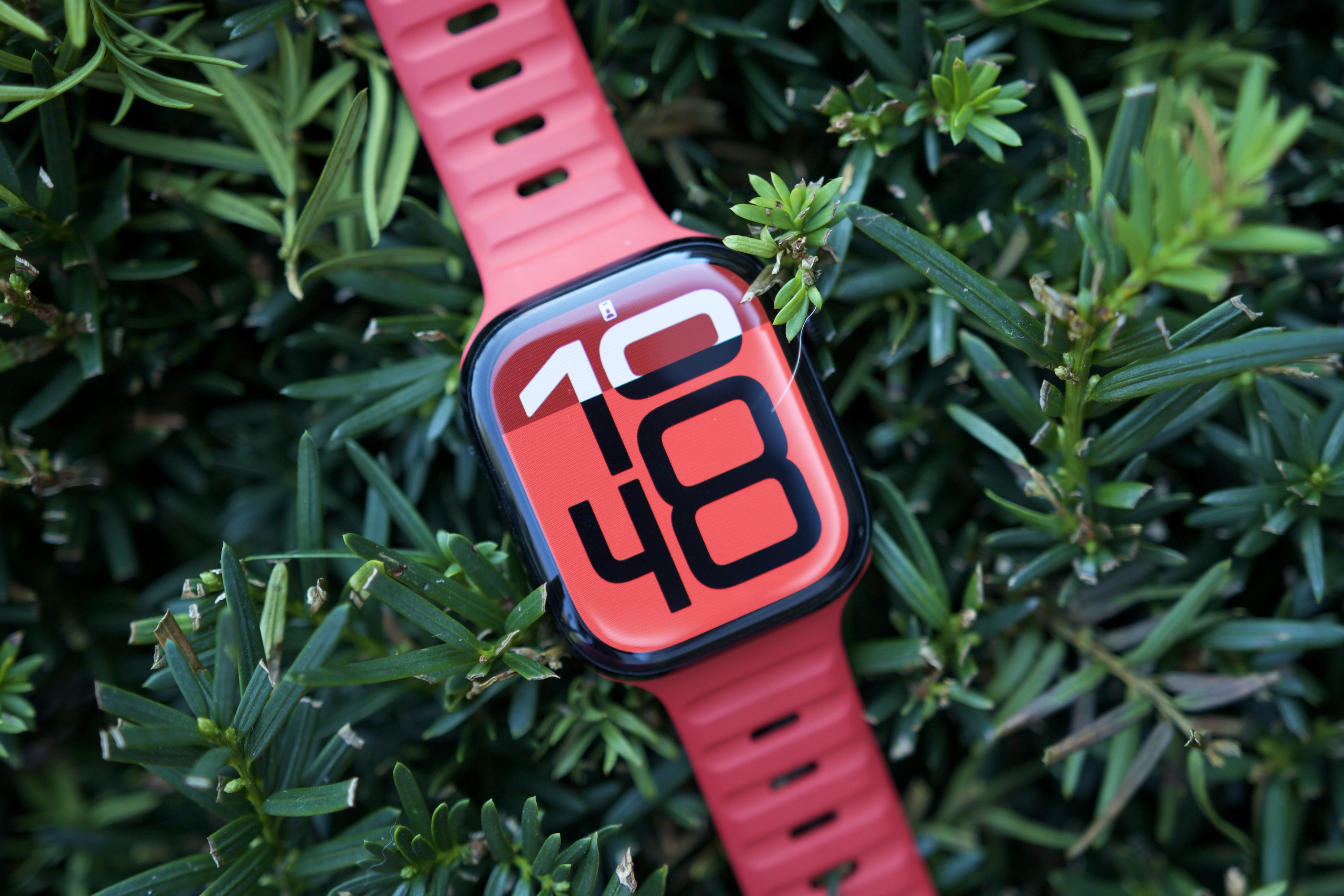 The Apple Watch Series 10 sitting on top of a green bush.