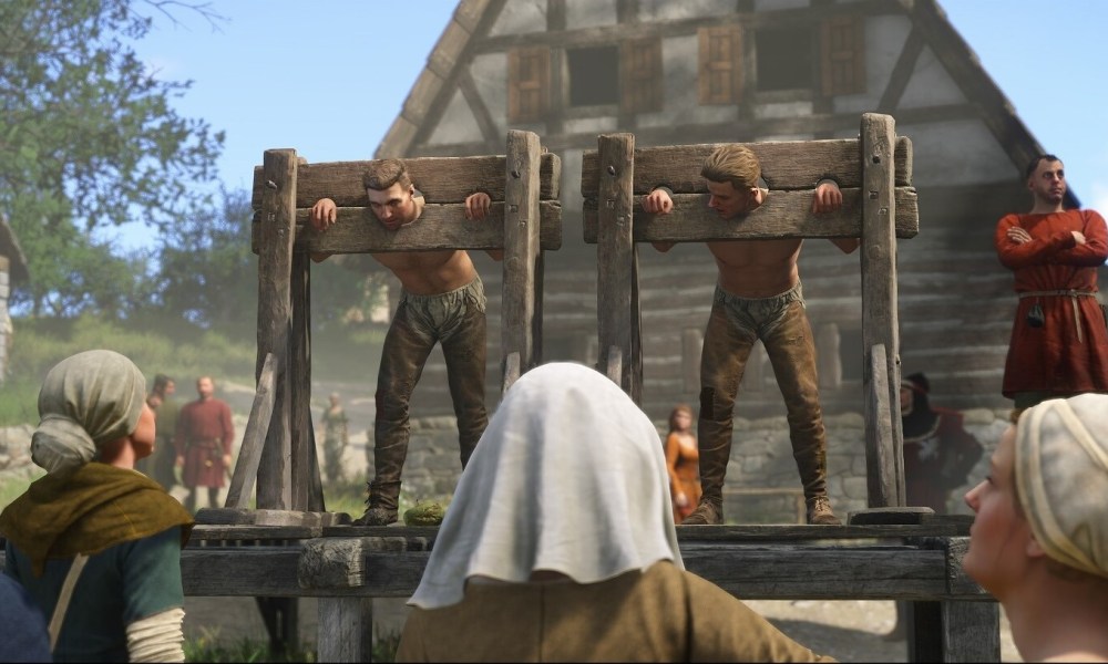 two men in wooden pillory on stage with crowd in front of them.