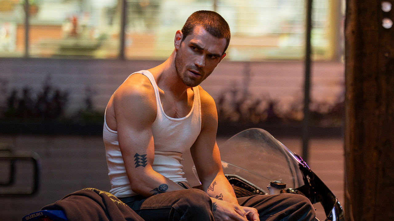 A young man with a shaved head and white tank top sits on a motorcycle in One Fast Move.