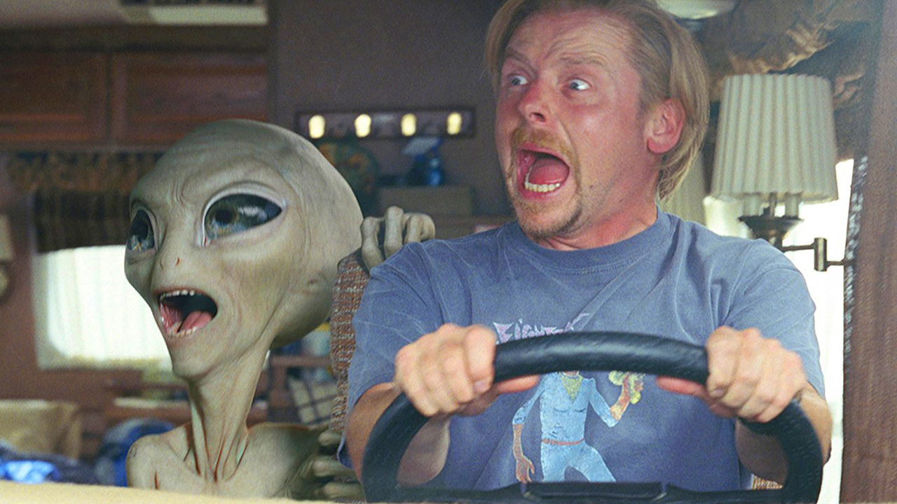 Simon Pegg driving a car with an alien beside him, both looking to the side and screaming in a scene from the movie Paul.