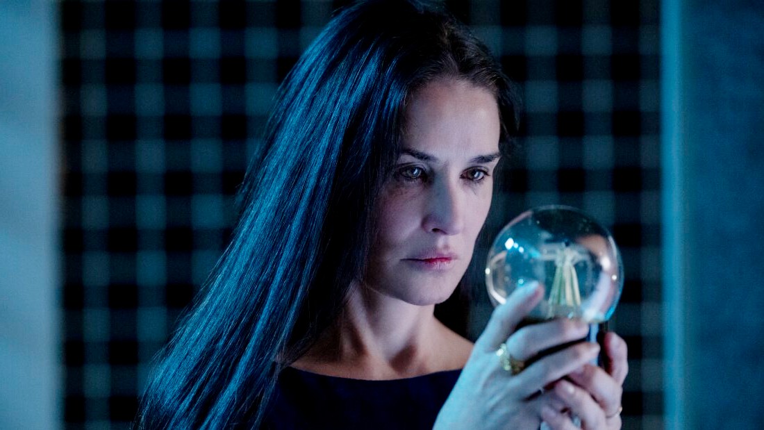 A woman looks at a snow globe in The Substance.