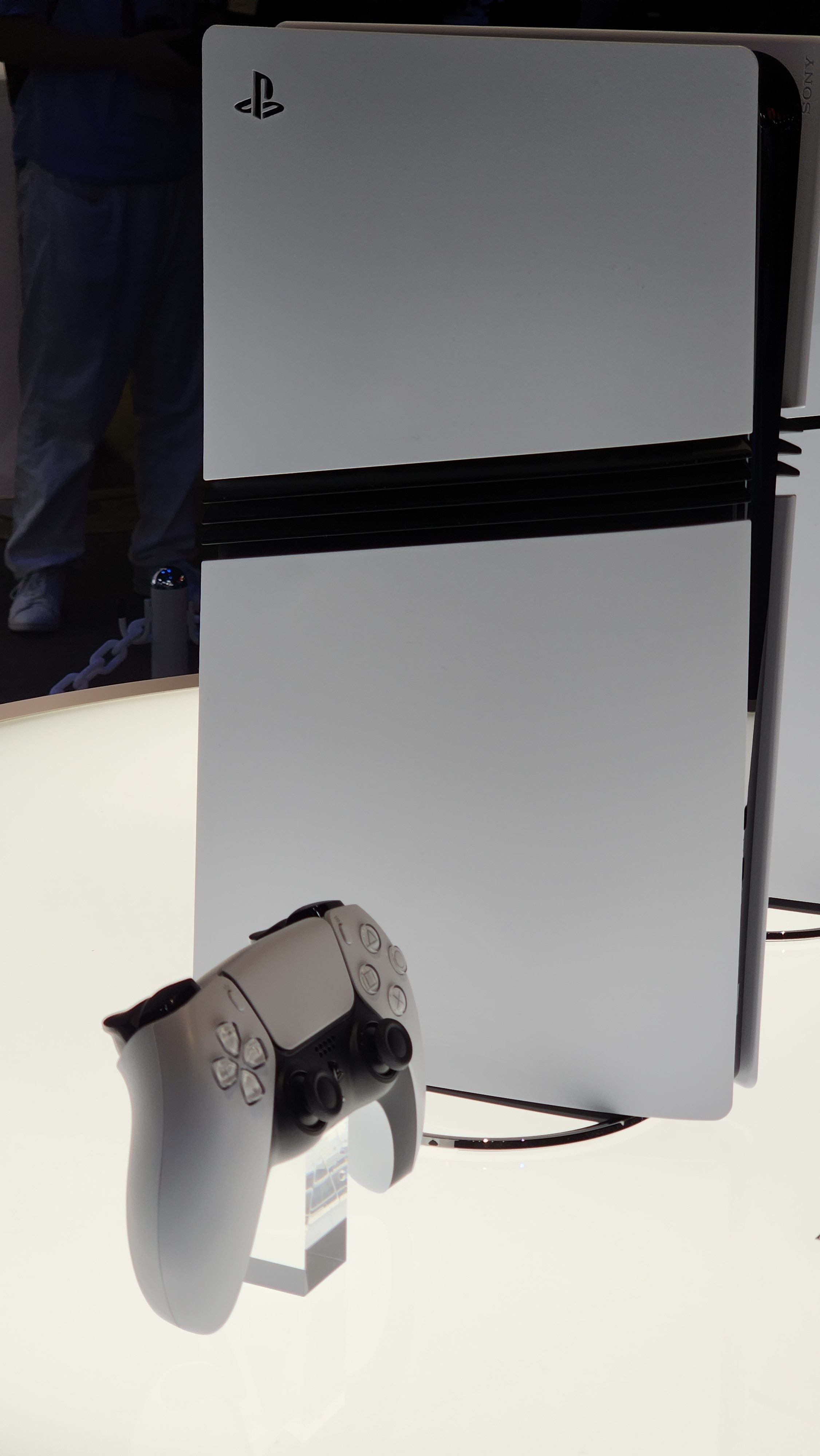 A side view of a vertical PS5 Pro, with a matching controller propped up next to it