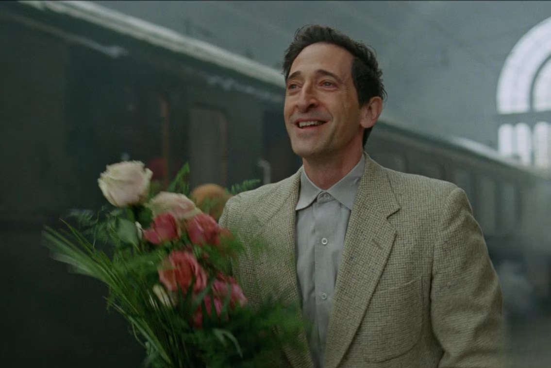 Adrien Brody carrega um buquê de flores em The Brutalist.