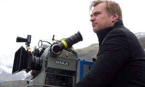 Christopher Nolan sits in front of an IMAX camera.