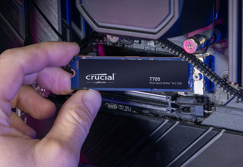 El SSD Crucial T705 PCIe 5.0 sostenido frente a una placa base. 