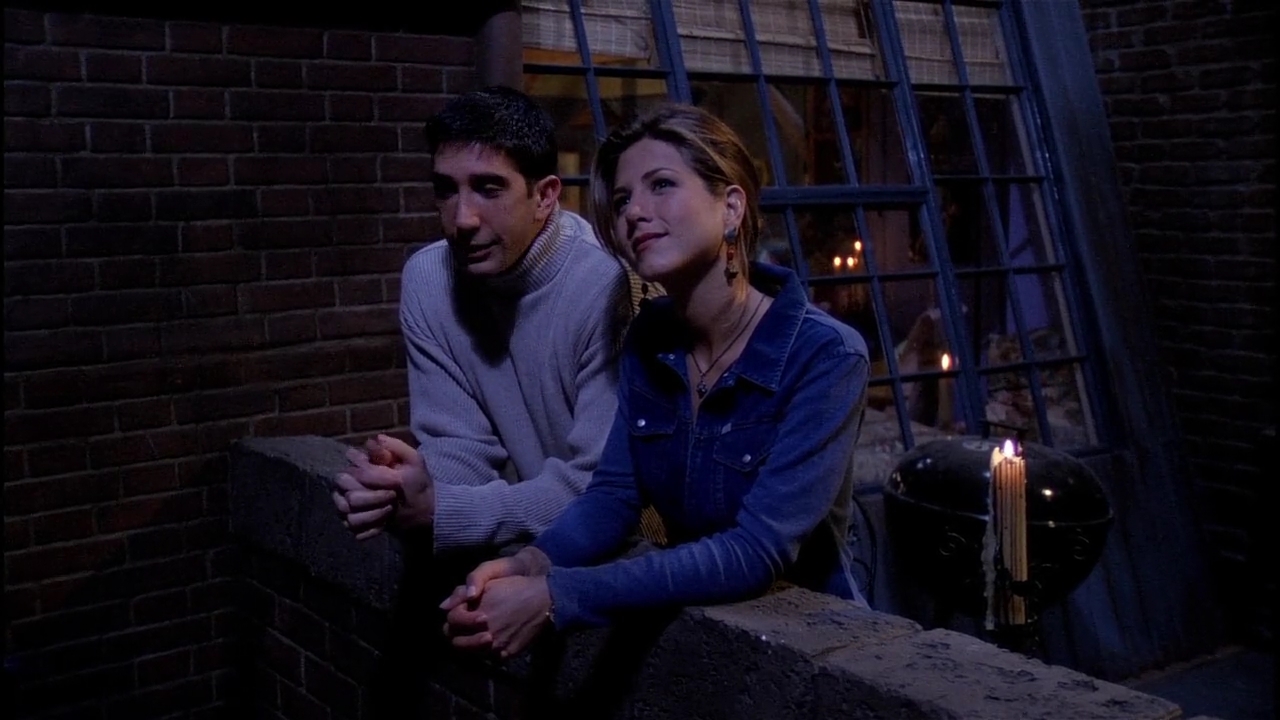 David Schwimmer et Jennifer Aniston dans le rôle de Ross et Rachel debout devant un balcon et levant les yeux dans Friends.