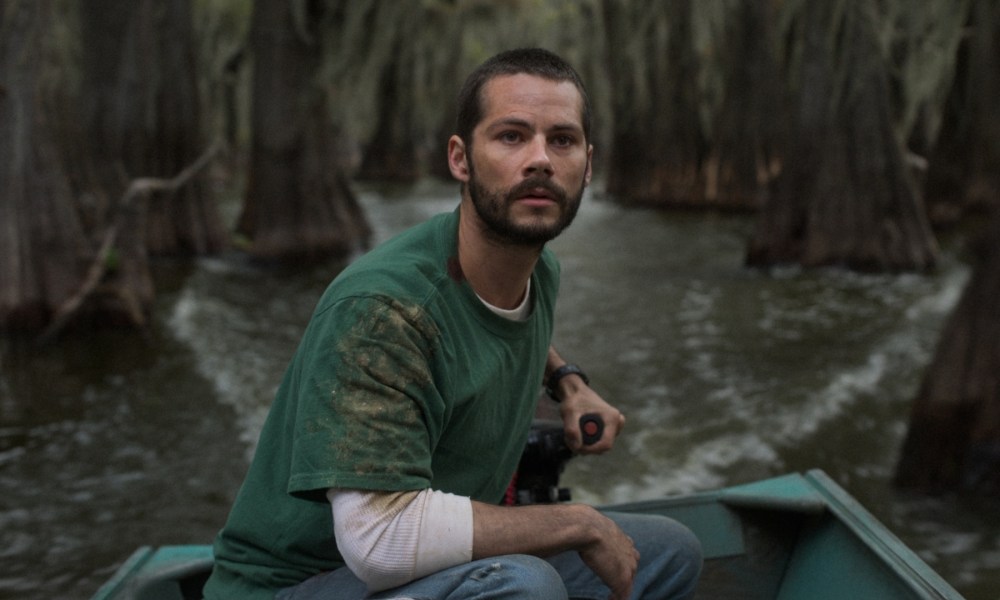 Dylan O'Brien sits in a boat and puts his hand on the lever.