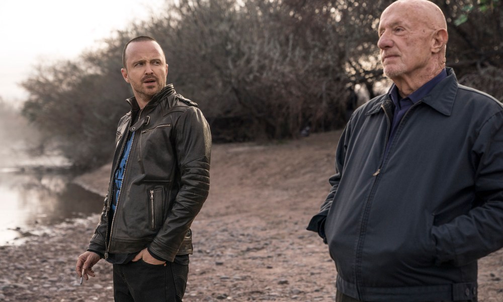 Two men stand next to each other by a lake.