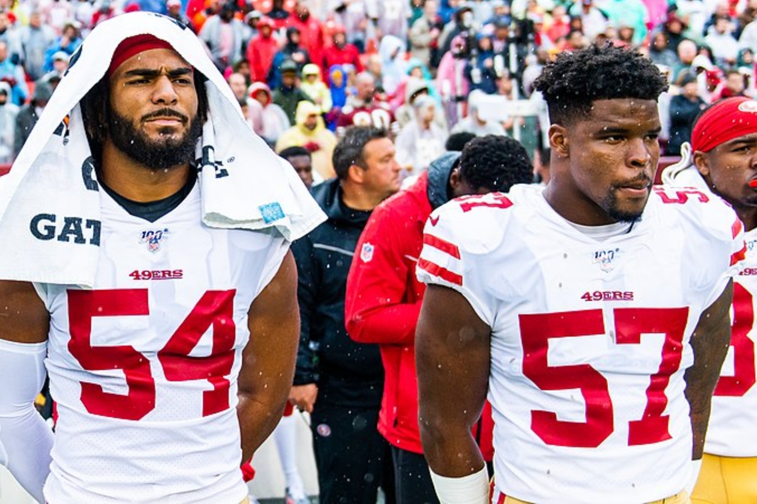 Two linebackers stand next to each other on the sidelines.