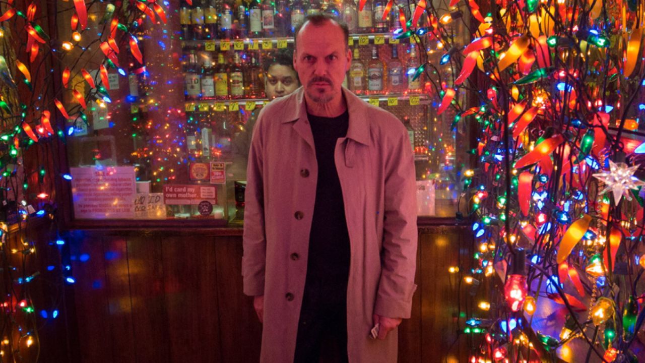 Michael Keaton como Riggan Thomson saindo de uma loja cheia de luzes em Birdman.