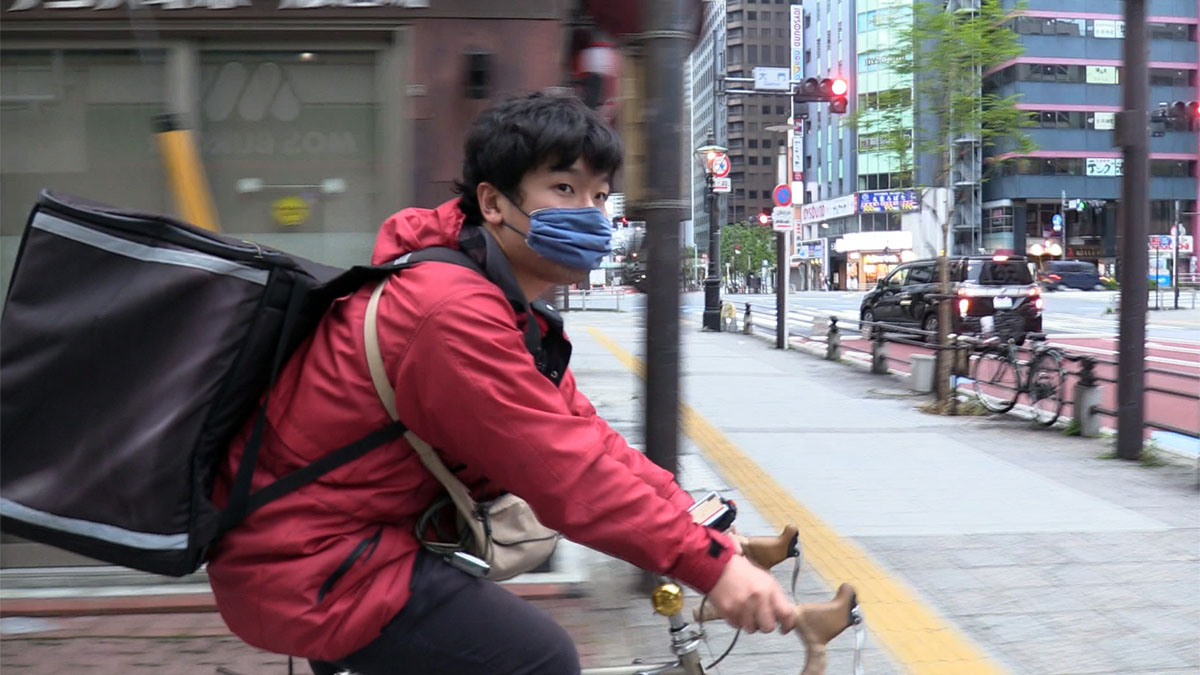 An UberEats deliveryman bikes through Tokyo in Tokyo Uber Blues.