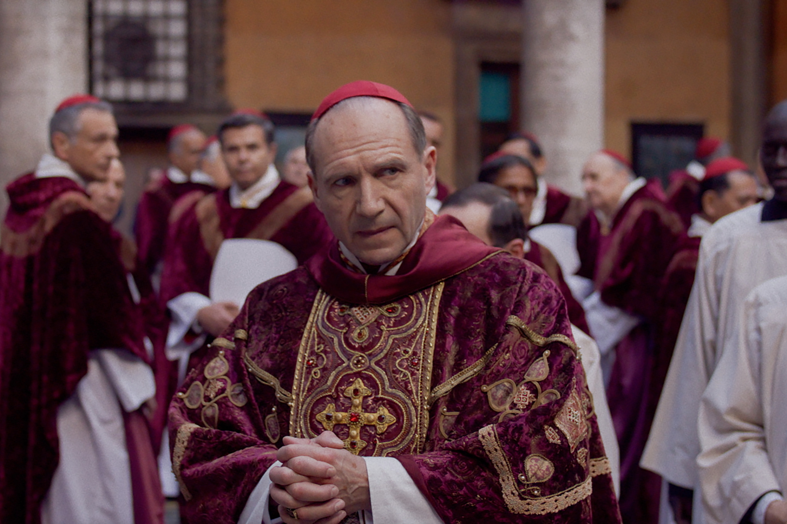 Ralph Fiennes walks through a crowd of Catholic Cardinals in Conclave.