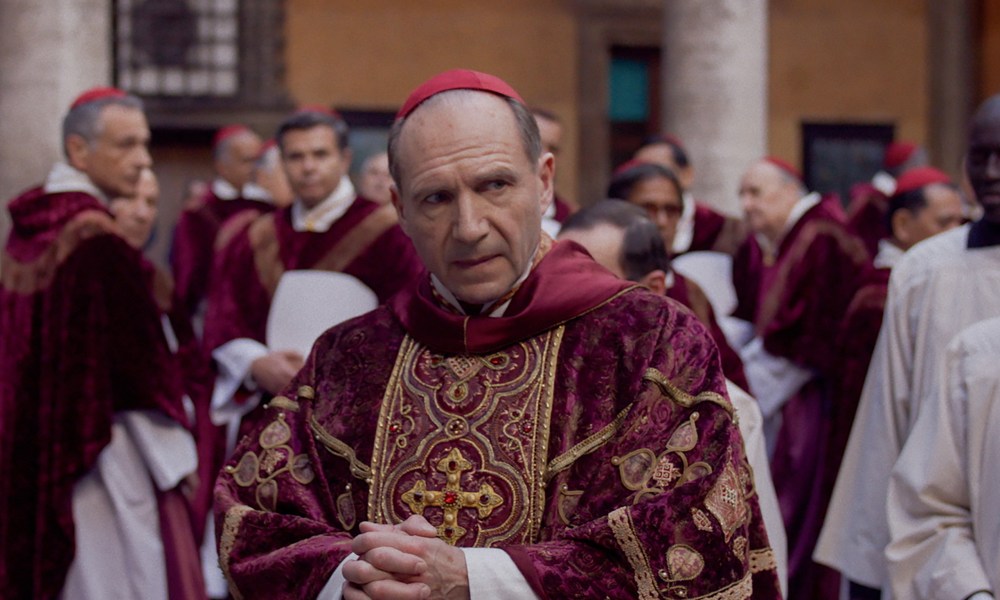 Ralph Fiennes walks through a crowd of Catholic Cardinals in Conclave.