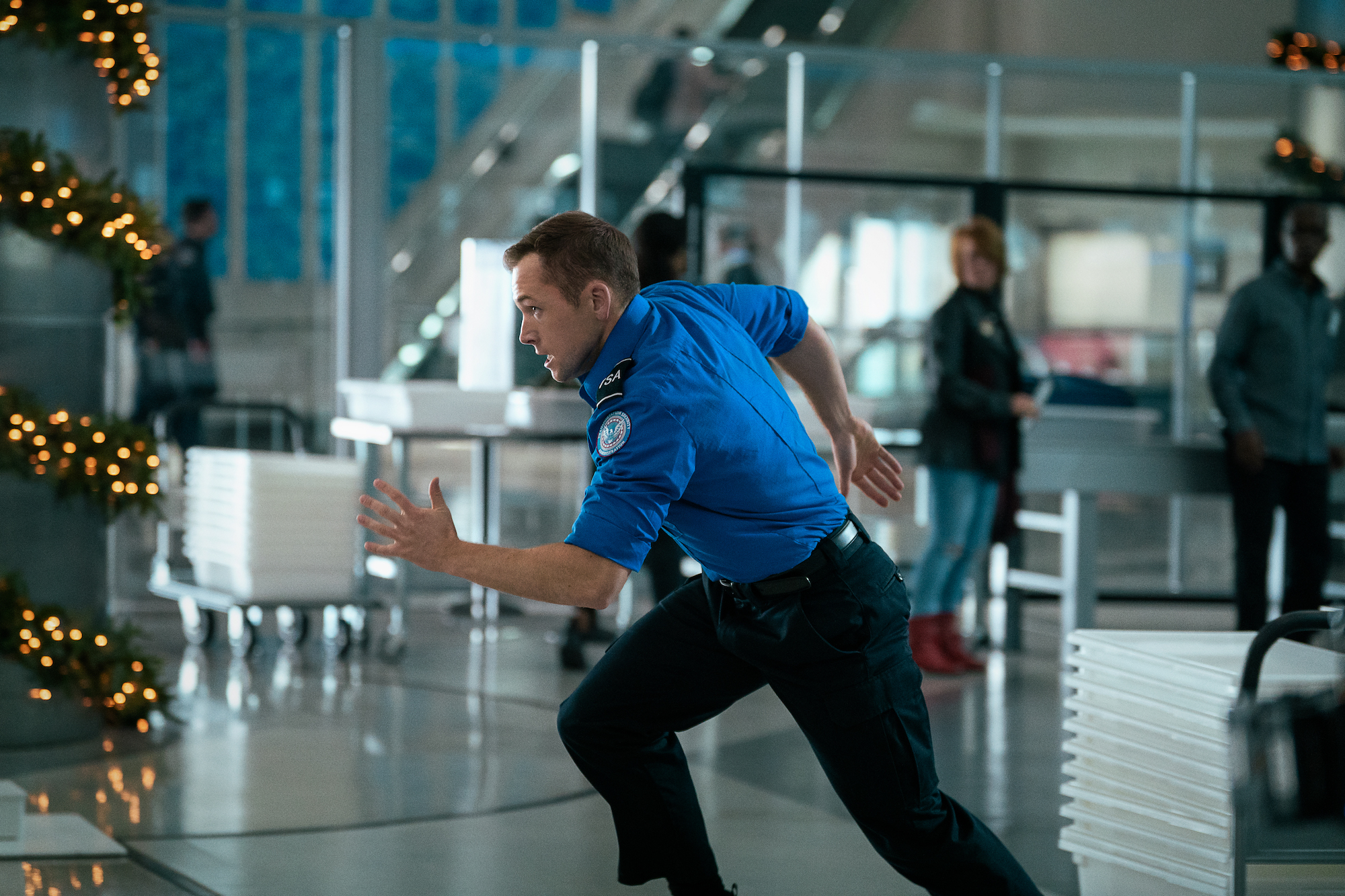 Taron Egerton sprinte dans un aéroport.