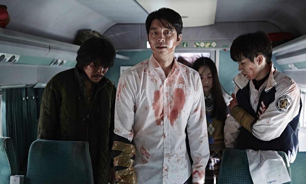 A man in a bloody shirt stands with passengers on a train.