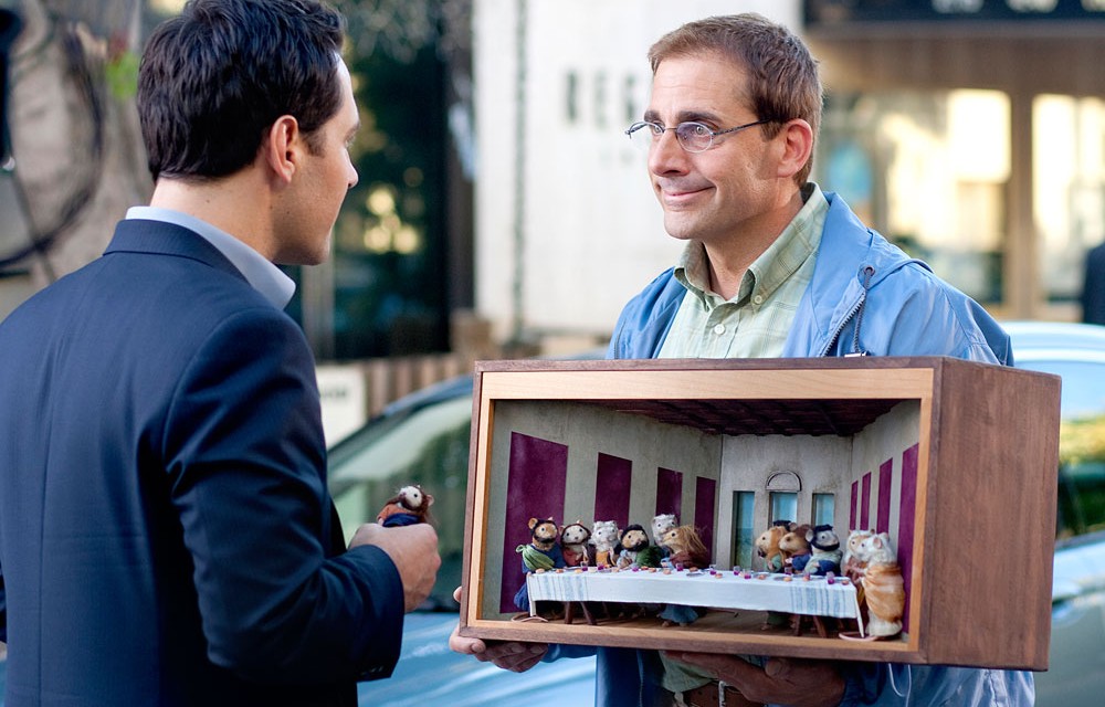 Un hombre sostiene un diorama en Cena para idiotas.