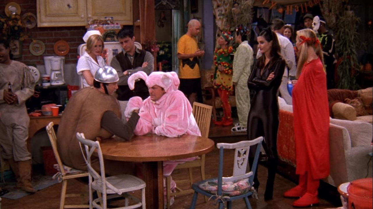 Ross in a Spud-nik costume, Chandler dressed as a pink bunny arm wrestling as others look on in Friends.