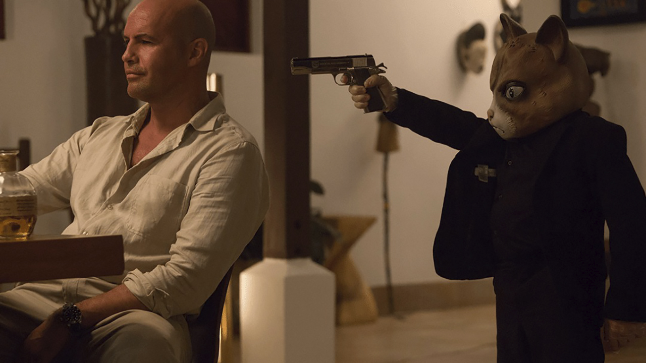 A little person in a fox mask holds a gun to the back of Billy Zane's head in Mad Dogs on Amazon Prime Video.