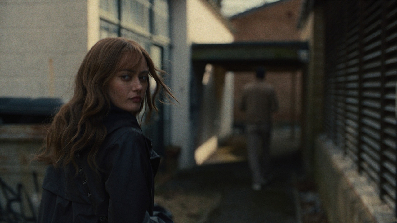 Ella Purnell walking down a dark alley, looking back behind her in Sweetpea.