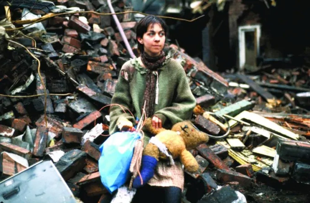 A woman sits on the rubble in Threads.