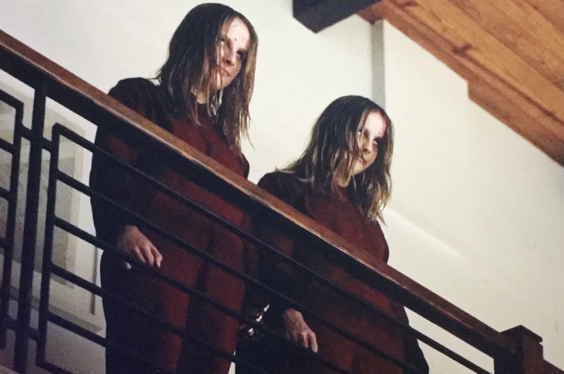 Two identical girls stand near a railing in Us.