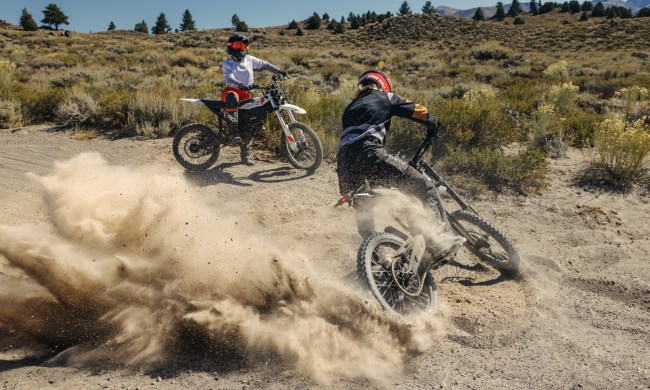 A rider sitting on a Zero XE watching another rider doing donuts in the dirt on a Zero XB.