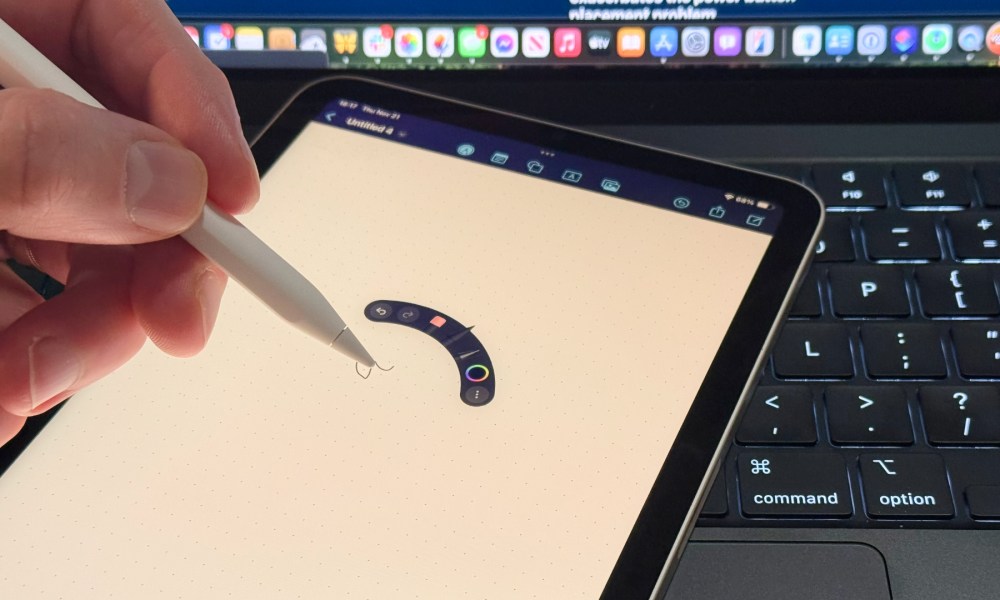 An Apple Pencil Pro being held in a person's left hand with squeeze controls showing on an iPad mini 7 on top of a MacBook Pro keyboard.