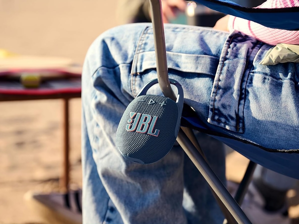 The JBL Clip 5 portable Bluetooth speaker attached to a chair at the beach.