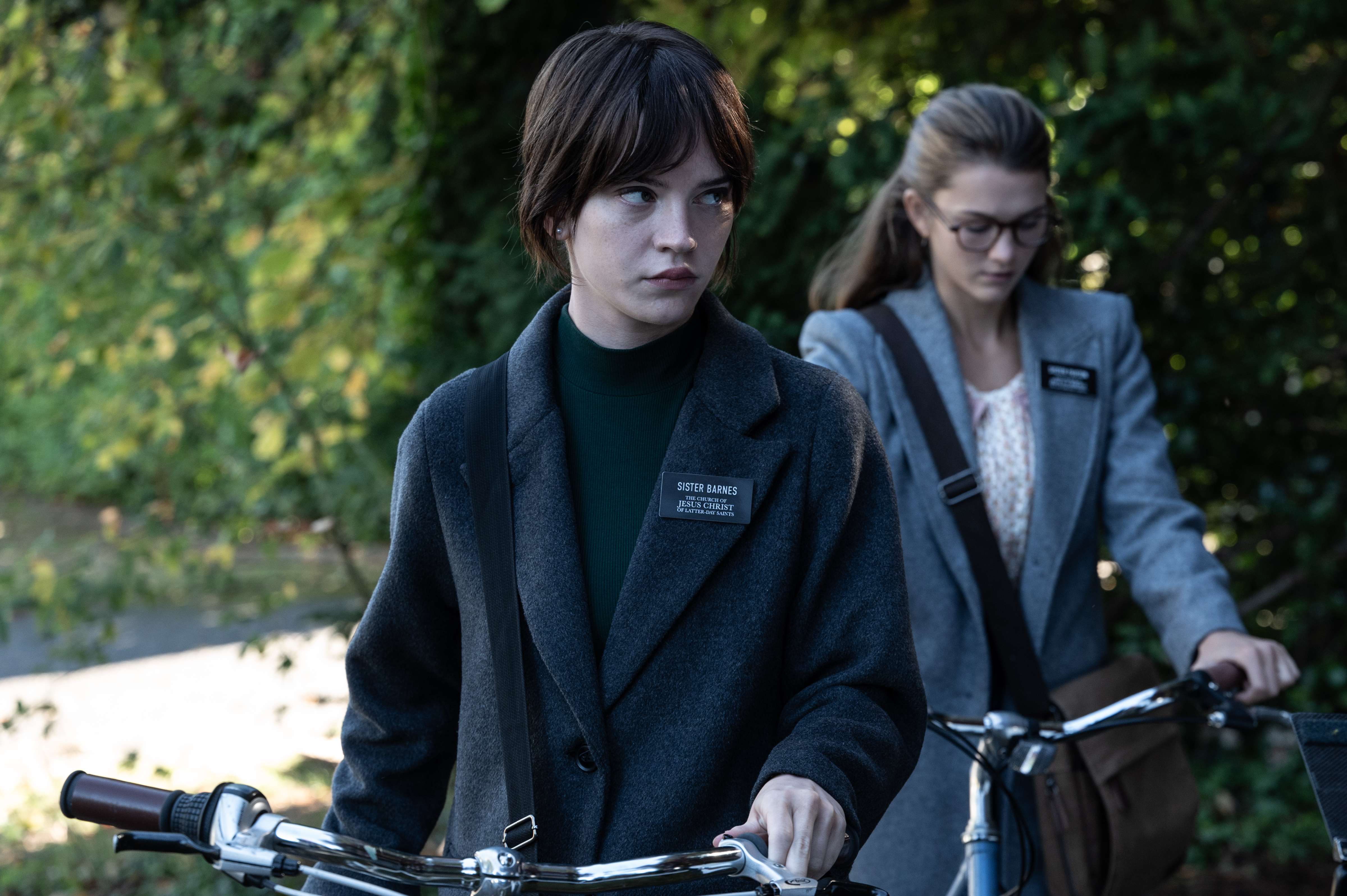 Duas meninas seguram suas bicicletas e caminham.