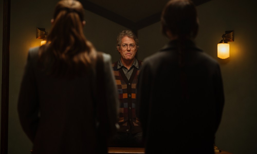 Hugh Grant stands in front of two women in Heretic.