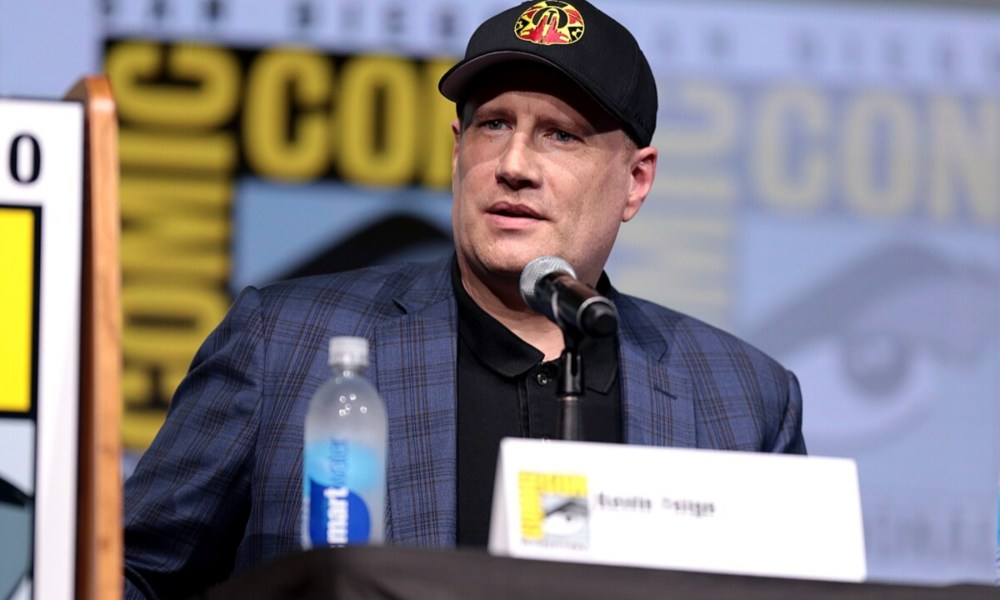 Kevin Feige sits at a podium in front of a mic.