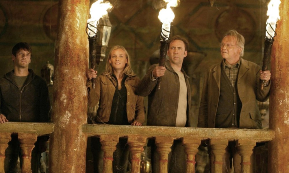 A group of four people stand above a rail and hold torches.